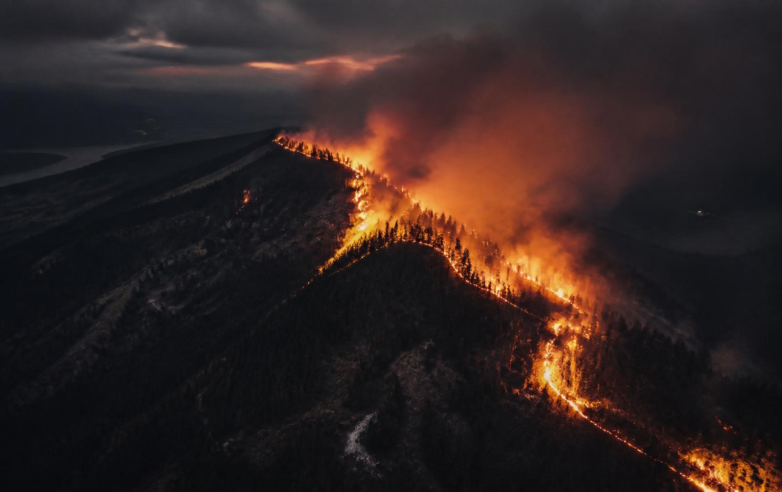 Aerial view of a wildfire burning along a forest ridge at dusk